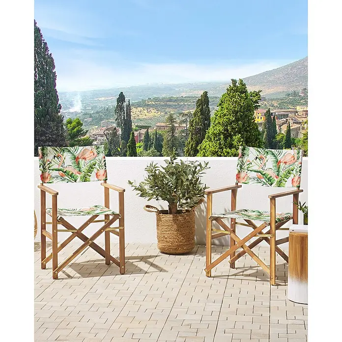 6er-Set Gartenstuhl CINE in Grün/Weiß/Rosa -  - Zwei hölzerne Regiestühle mit Flamingo- und Tropenblattmusterstoff auf einer Terrasse mit Blick auf ein malerisches Tal.