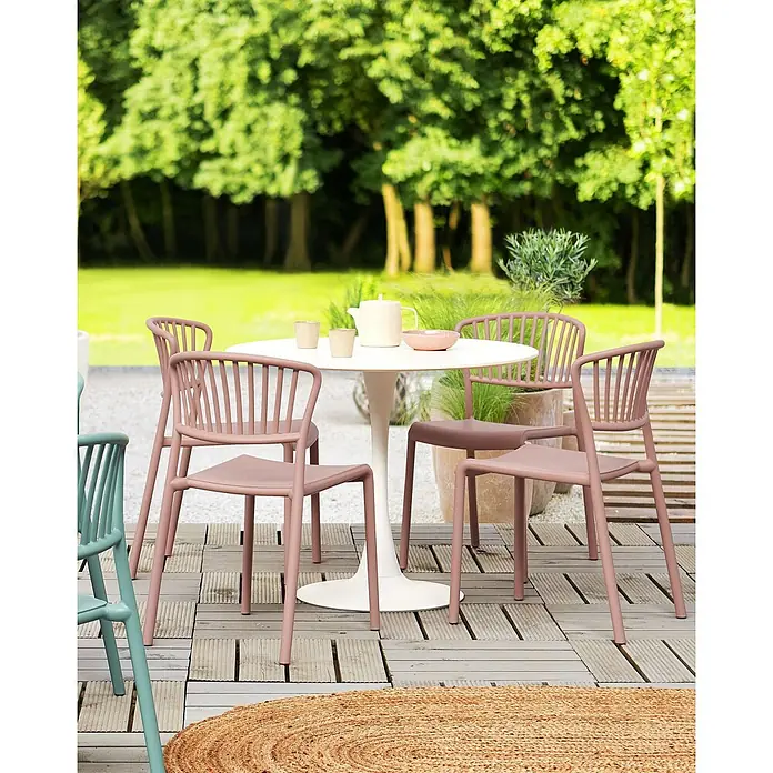 4er-Set Esszimmerstuhl GELA in Rosa -  - Ein Outdoor-Esstisch mit weißem Rundtisch und mehreren rosa Stühlen auf einer Terrasse, teils mit blaugrünem Stuhl und Juteteppich.
