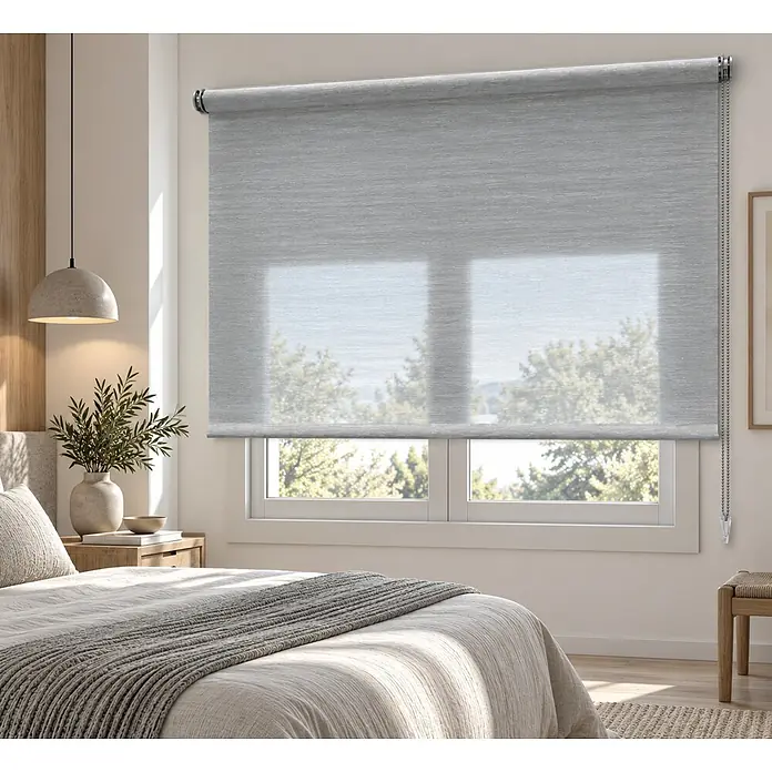 Estor enrollable Icaro - An x Al: 135 x 250 cm, Gris - Estor enrollable gris claro semitransparente instalado en una ventana de dormitorio, parcialmente bajado, revelando los árboles exteriores.