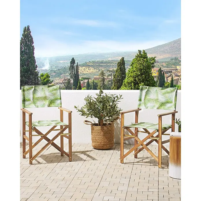 6er-Set Gartenstuhl CINE in Grün/Weiß/Braun -  - Zwei Regiestühle aus Holz mit grünem Palmenblattmuster stehen auf einer gefliesten Terrasse mit Blick auf ein malerisches Tal.