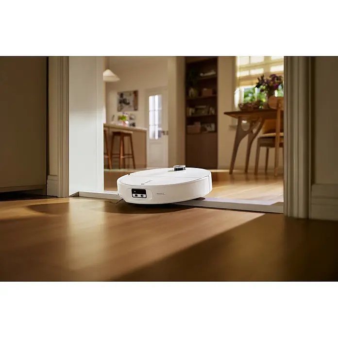 Roborock Saugwischroboter Qrevo Edge 2X - Saugkraft: 25.000 Pa, Akkulaufzeit: 188 min, Fassungsvermögen Roboter: 240 ml, Weiß - Ein weißer Saugroboter überquert reibungslos eine Schwelle von einem dunkleren Raum in einen helleren Wohnbereich mit Holzboden.