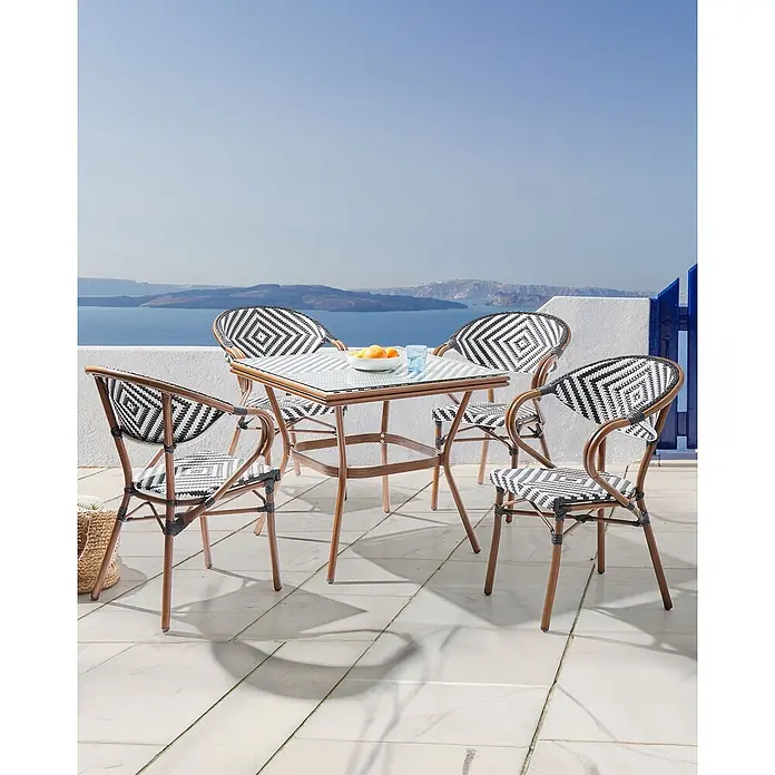 4er-Set Gartenstuhl CASPRI in Schwarz/Weiß/Braun -  - Ein Outdoor-Essset mit quadratischem Glastisch und vier Stühlen mit schwarz-weiß geflochtenen Sitzen und braunen Gestellen auf einem Balkon mit Meerblick.