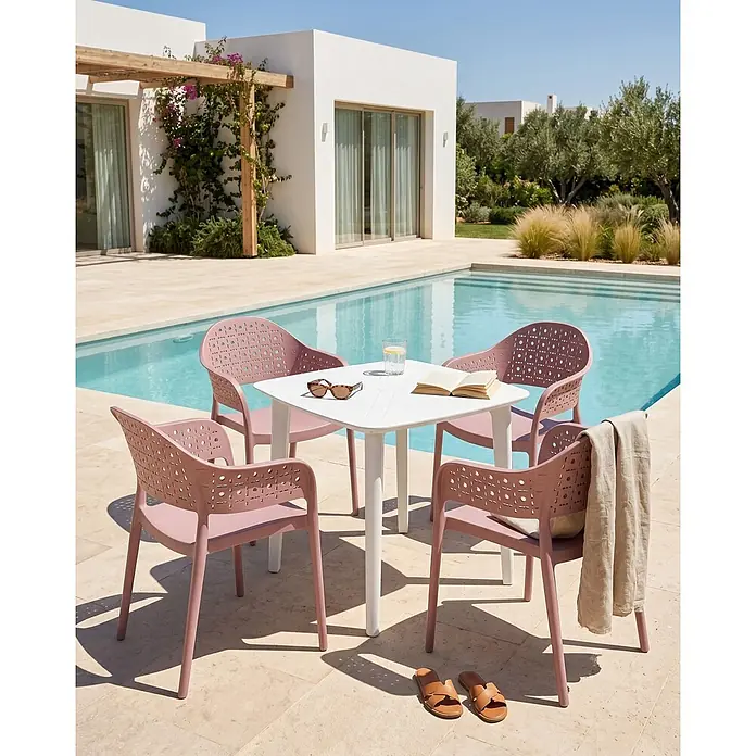 4er-Set Esszimmerstuhl NARINO in Rosa -  - Quadratischer weißer Tisch und vier staubrosafarbene Plastikstühle mit perforierten Rückenlehnen neben einem Pool.