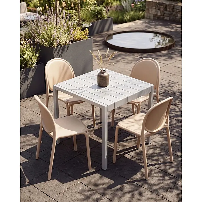 4er-Set Esszimmerstuhl BRUGNELLO in Beige -  - Quadratischer hellgrauer Gartentisch mit vier beigen Stühlen auf einer Terrasse mit Pflanzen.