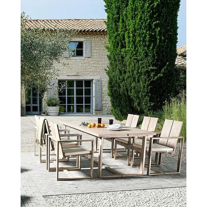 Beliani Gartenstuhl-Set AZZANELLO - 6 Stk., Akazienholz, Braun, B x T x H: 63 x 61 x 90 cm - Outdoor-Essgruppe mit Holztisch und sechs Stühlen auf einer gepflasterten Terrasse vor einem Steinhaus.