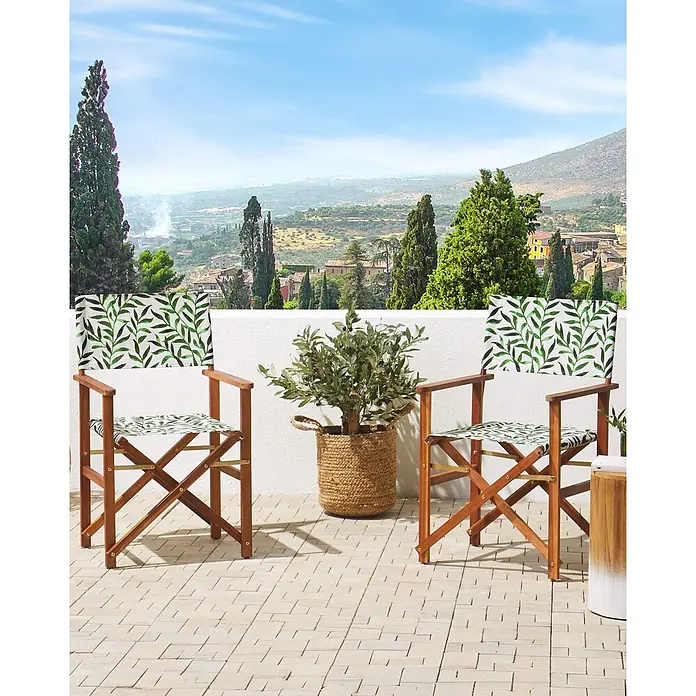 6er-Set Gartenstuhl CINE in Grün/Bunt/Braun -  - Zwei Regiestühle aus Holz mit grünem Blattmusterstoff stehen auf einer Terrasse mit Landschaftsblick.