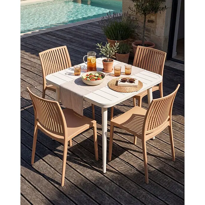 4er-Set Gartenstuhl ILLUMANI in Beige -  - Weißer Gartentisch mit vier hellbraunen Stühlen auf einer Holzterrasse am Pool, gedeckt für eine Mahlzeit.