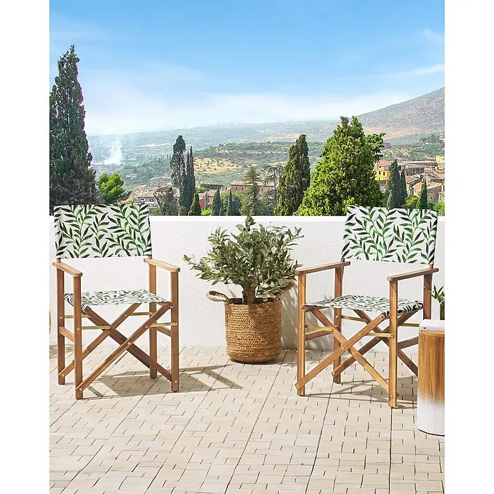 6er-Set Gartenstuhl CINE in Grün/Weiß/Braun -  - Zwei Holz-Regiestühle mit grünem Blättermuster auf der Terrasse, flankiert von einem Olivenbaum und Blick auf eine Landschaft.