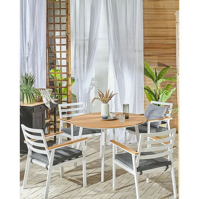 Beliani Gartenstuhl-Set CAVOLI - 4 Stk., Aluminium, Weiß, B x T x H: 54 x 60 x 82 cm - Eine Outdoor-Essgruppe mit rundem Holztisch und vier weißen Stühlen mit grauen Kissen und Holzarmlehnen auf einer Terrasse.