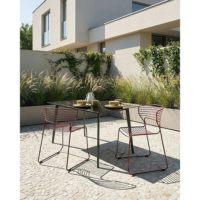Beliani Gartenstuhl-Set PISTOIA - 2 Stk., Stahl, Rot, B x T x H: 54 x 51 x 80 cm - Rote Drahtstühle und ein schwarzer Esstisch im Freien auf einer Terrasse.
