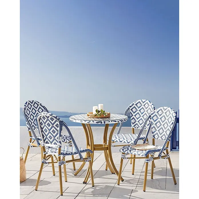 4er-Set Gartenstuhl RIFREDDO in Blau/Beige/Weiß -  - Blau-weiß geflochtene Terrassen-Essgruppe mit Glastisch und vier Stühlen, goldfarbene Gestelle, auf einer Terrasse mit Meerblick.