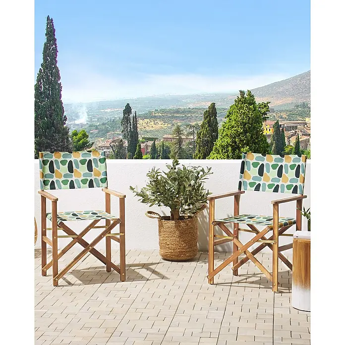 6er-Set Gartenstuhl CINE in Grün/Bunt/Grün -  - Zwei hölzerne Regiestühle mit farbig gemustertem Stoffbezug, die eine Olivenpflanze in einem Korb auf einer Terrasse mit Aussicht flankieren.