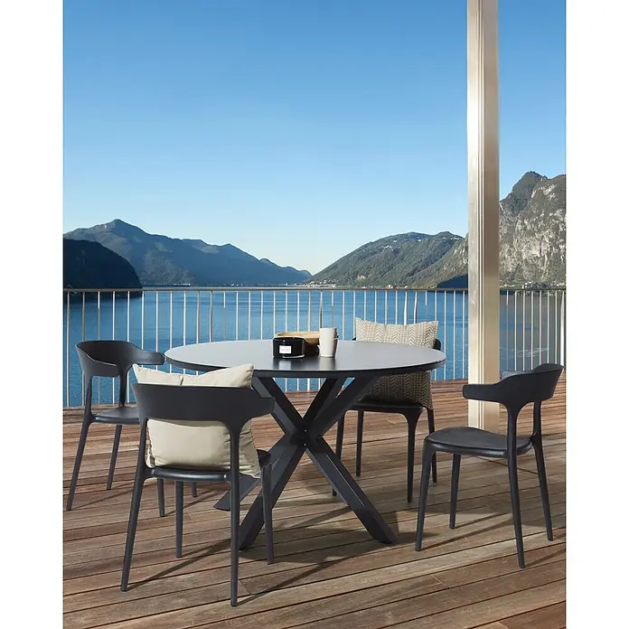 4er-Set Gartenstuhl GUBBIO in Schwarz -  - Ein runder, dunkler Esstisch mit Sternfuß und vier passenden dunklen Stühlen mit Kissen auf einem Holzbalkon mit Seeblick.