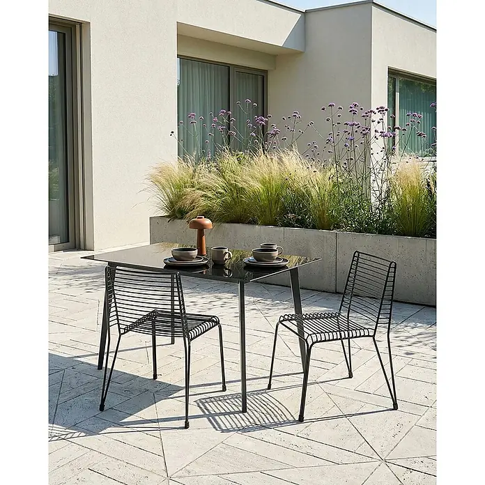 Beliani Gartenstuhl-Set CHIEVE - 2 Stk., Stahl, Schwarz, B x T x H: 49 x 57 x 80 cm - Schwarzer Außentisch und zwei Metallstühle auf einer Terrasse, zum Essen gedeckt, umgeben von Pflanzen.