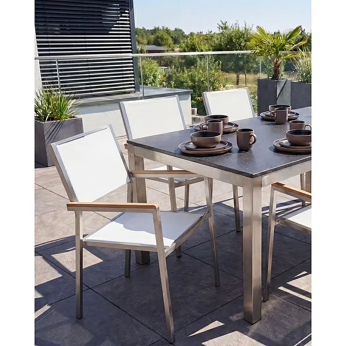6er-Set Gartenstuhl GROSSETO in Weiß/Silber/Braun -  - Eine Outdoor-Essgruppe aus gebürstetem Edelstahl mit dunkler Tischplatte und passenden Stühlen mit weißen Stoffbezügen und Holzarmlehnen, auf einer sonnigen Terrasse.