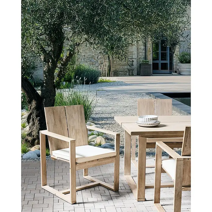 Beliani Gartenstuhl-Set AZZANELLO - 2 Stk., Akazienholz, Braun, B x T x H: 63 x 61 x 90 cm - Helle hölzerne Outdoor-Essgruppe mit weißen Kissen auf einer gepflasterten Terrasse, mit Tellern auf dem Tisch, umgeben von einem Garten und Olivenbaum.