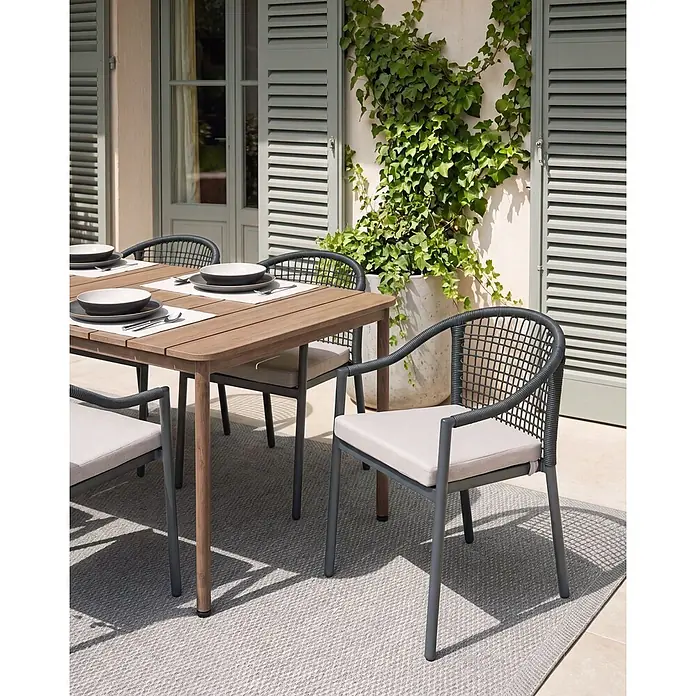 Beliani Gartenstuhl-Set OZZERO - 4 Stk., Aluminium, Schwarz, B x T x H: 55 x 60 x 76 cm - Outdoor-Esstisch-Set: Holztisch und dunkelgraue Stühle mit geflochtenen Details und hellen Kissen auf einer Terrasse.