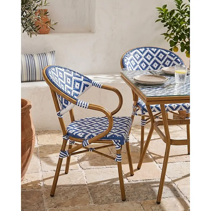 4er-Set Gartenstuhl CASPRI in Weiß/Blau/Braun -  - Essgruppe für draußen mit Stühlen und Tisch, blau-weiß gemustertem Geflecht und hellem Holzrahmen, auf einer Steinterrasse.