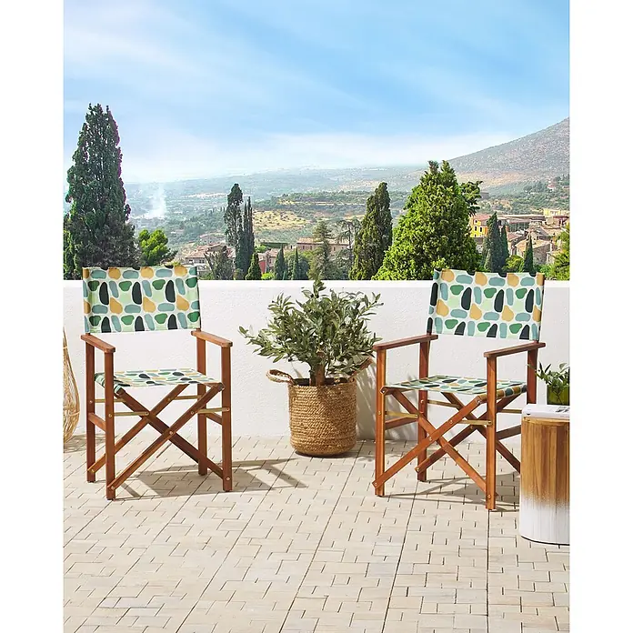 6er-Set Gartenstuhl CINE in Bunt/Grün/Orange -  - Zwei klappbare Regiestühle aus Holz mit bunten, abstrakt gemusterten Stoffbezügen stehen auf einer Terrasse mit Landschaftsblick.