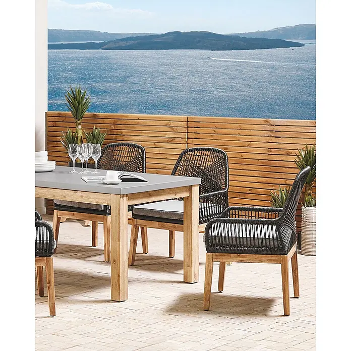 Beliani Gartenstuhl-Set OLBIA - 2 Stk., Akazienholz, Schwarz, B x T x H: 64 x 71 x 89 cm - Outdoor-Essgruppe mit grauem Tisch und schwarzen Flechtstühlen auf einer Terrasse am Meer.