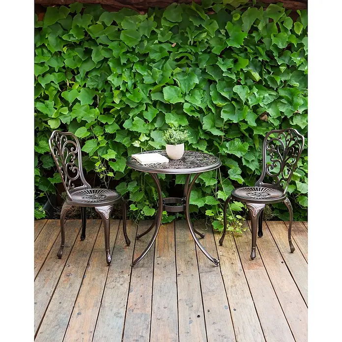 Beliani Gartenstuhl-Set TRIORA - 2 Stk., Aluminium, Braun, B x T x H: 50 x 50 x 88 cm - Elegantes bronzefarbenes Outdoor-Bistro-Set mit Tisch und zwei Stühlen auf einer Holzterrasse, umgeben von dichtem Grün.