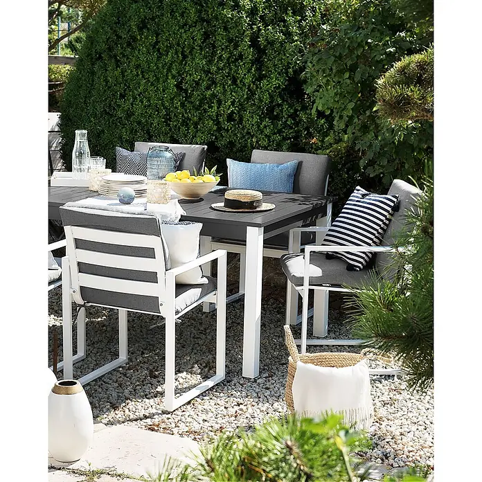 4er-Set Gartenstuhl PANCOLE in Grau/Weiß -  - Eine Outdoor-Essgruppe mit einem dunkelgrauen Tisch und weißen Stühlen mit grauen Kissen und gestreiften Polstern auf einer Kiesterrasse.