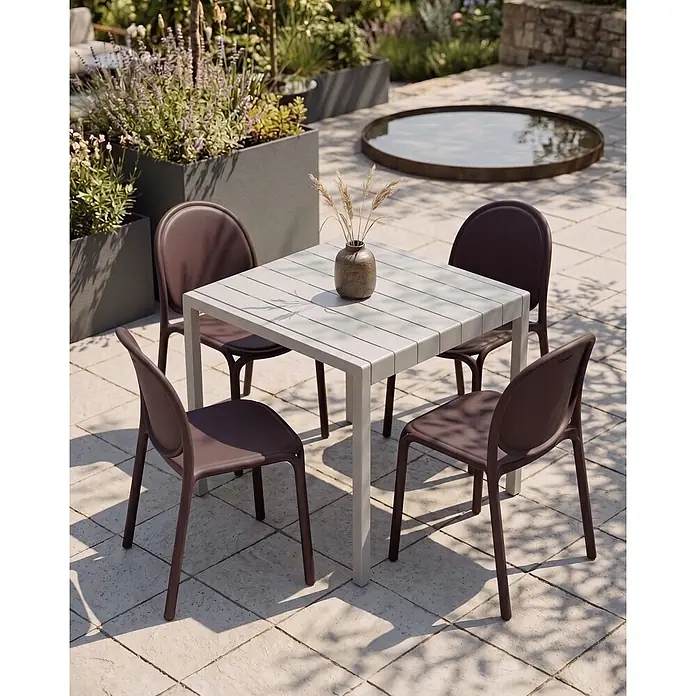 4er-Set Esszimmerstuhl BRUGNELLO in Braun -  - Hellesgrauer Latten-Gartentisch mit vier dunkelbraunen Stühlen auf gepflasterter Terrasse, umgeben von Pflanzen.
