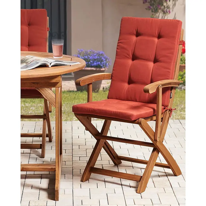 Beliani Gartenstuhl-Set MAUI PREMIUM - 2 Stk., Akazienholz, Klappbar, Braun, B x T x H: 46 x 48 x 92 cm - Eine Essgruppe aus Holz für den Außenbereich mit rot-orangen Polstern, rundem Tisch und Klappstuhl auf einer Terrasse.