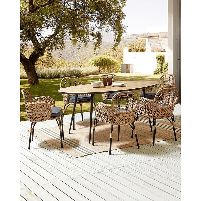 12er-Set Gartenstuhl PRATELLO in Naturfarben/Beige/Grau -  - Outdoor-Essgruppe: ovaler Holztisch mit schwarzen Beinen, sechs geflochtene Rattan-Stühle mit dunklen Kissen auf einem Terrassenteppich.