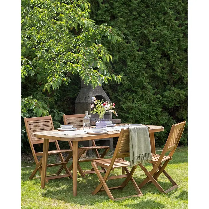 4er-Set Gartenstuhl PARAGGI in Braun -  - Ein hölzernes Garten-Essset mit vier Klappstühlen, die geflochtene Rückenlehnen im Rattan-Stil haben, in einem grünen Garten.