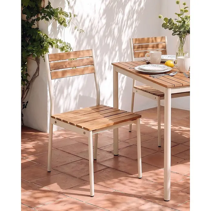 Beliani Gartenstuhl-Set CORRICELLA - 2 Stk., Akazienholz, Braun, B x T x H: 47 x 54 x 90 cm - Gartentisch und Stühle mit Holzlatten und hellem Metallgestell auf einer sonnigen Terrasse.
