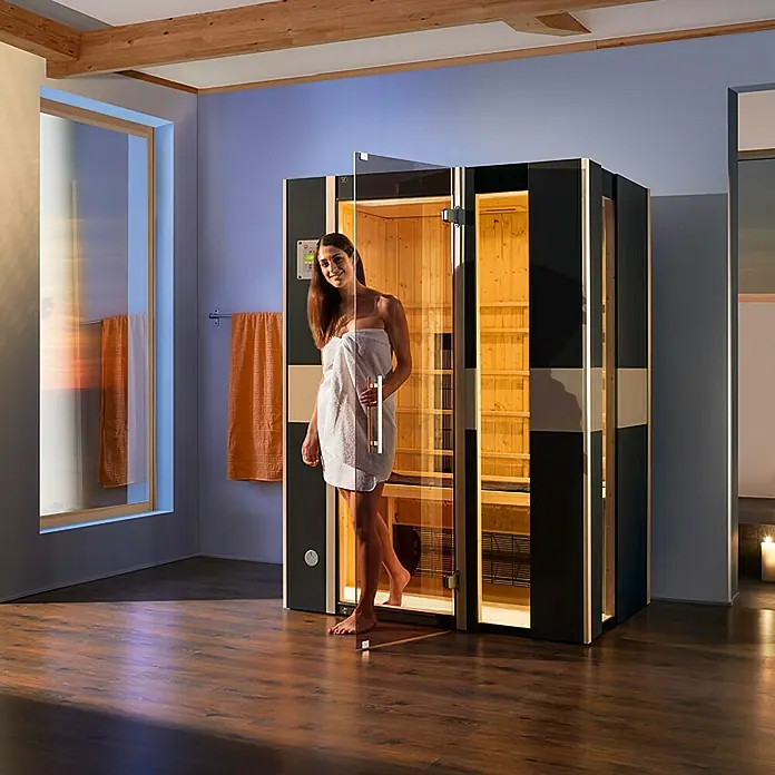 Weka Infrarotkabine Mila 2 - 2.050 W, 5 Keramikstrahler, 100 x 137 x 190 cm - Frau verlässt die Sauna, gehüllt in ein Handtuch, das moderne Design und die entspannende Atmosphäre hervorhebt.