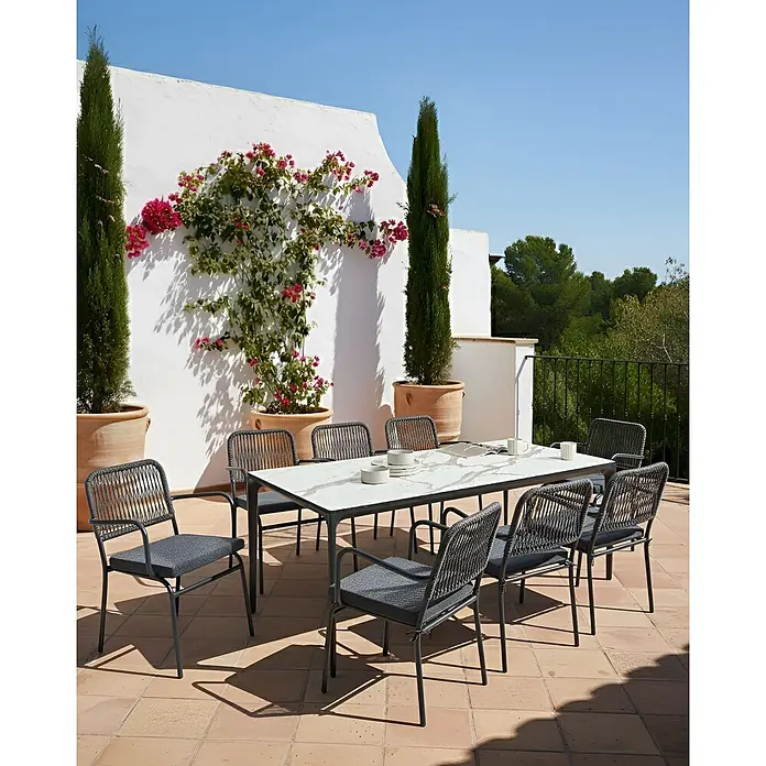 16er-Set Gartenstuhl TACENO in Grau -  - Esstischgruppe für draußen auf einer sonnigen Terrasse, mit weißer Marmor-Tischplatte und dunklen Stühlen mit Geflechtlehnen, bereit für Mahlzeiten im Freien.