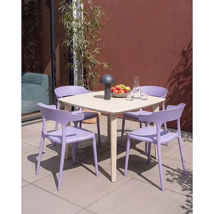4er-Set Gartenstuhl GUBBIO in Violett -  - Ein quadratischer beiger Gartentisch mit vier lavendelfarbenen Stühlen auf einer Terrasse, dekoriert mit Obst, einer Wasserkaraffe und einer kleinen Lampe.