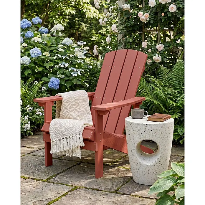 Gartenstuhl ADIRONDACK in Rot - (W) 75 x (H) 88 x - L - Rotbrauner Adirondack-Stuhl mit gemusterter Decke, daneben ein strukturierter Beistelltisch mit Tasse und Buch, auf einer Steinterrasse im Garten.