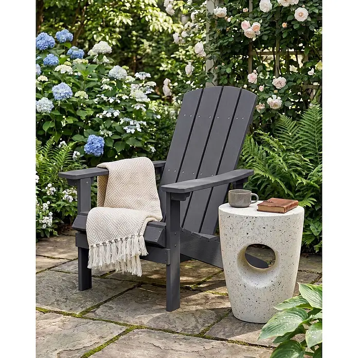 Gartenstuhl ADIRONDACK in Grau - (W) 75 x (H) 88 x - L - Dunkelgrauer Adirondack-Stuhl mit beiger Decke im Garten auf einer Steinterrasse.