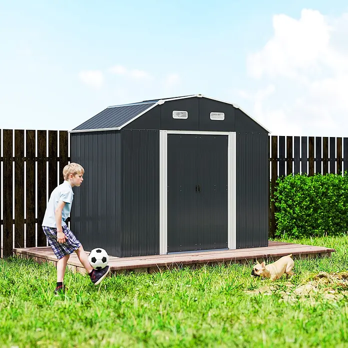 Outsunny Gerätehaus - Außenmaß inkl. Dachüberstand (B x T): 238 x 132 cm, Stahl, Dunkelgrau - Großer dunkelgrauer Metallgartenhaus mit weißer Zierleiste auf Holzterrasse im Garten, mit spielendem Jungen in der Nähe.