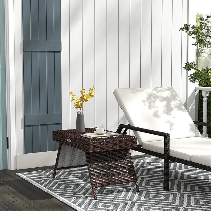 Furnicato Garten-Loungetisch - L x B x H: 60 x 41 x 41 cm, Braun - Brauner Flecht-Beistelltisch mit Vase und Buch, auf einem Outdoor-Teppich neben einer Liege.