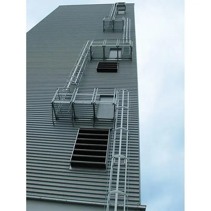 MUNK ortsfeste Steigleitern Stahl verzinkt, 4,76m SH -  - Mehrere silberne Metall-Zugangsleitern mit Sicherheitskäfigen und Podesten ermöglichen den vertikalen Zugang an der Wellblechfassade eines hohen Gebäudes.