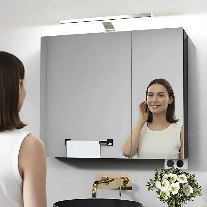 kalb Material für Möbel LED-Spiegelleuchte Innen - 3,7 W, L x B x H: 34 x 18,5 x 4 cm, Silbergrau - Eine Frau nutzt einen modernen Badspiegelschrank mit integrierter Beleuchtung, zwei Spiegeltüren, Handtuchhalter und Steckdose.