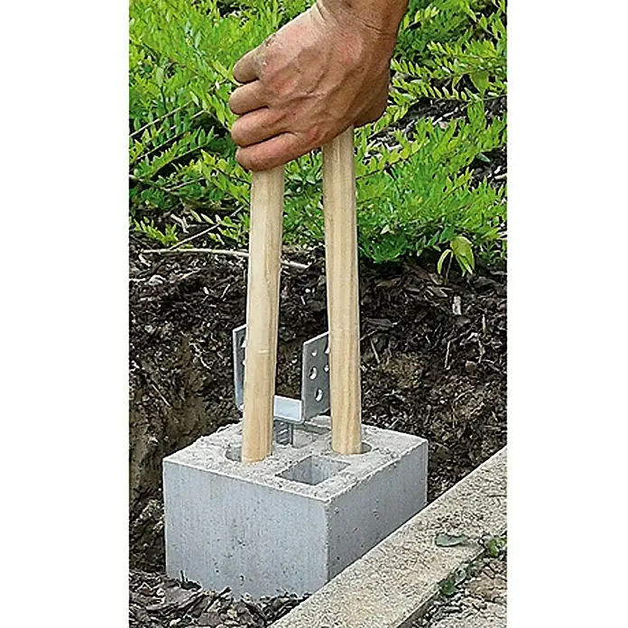 Christoph Zaun-Fundamentstein 4in1 - Grau, 19 x 19 x 25 cm, Beton - Nahaufnahme einer Person, die zwei Holzpfosten in einem Betonblock mit einem Metallpfostenträger befestigt.