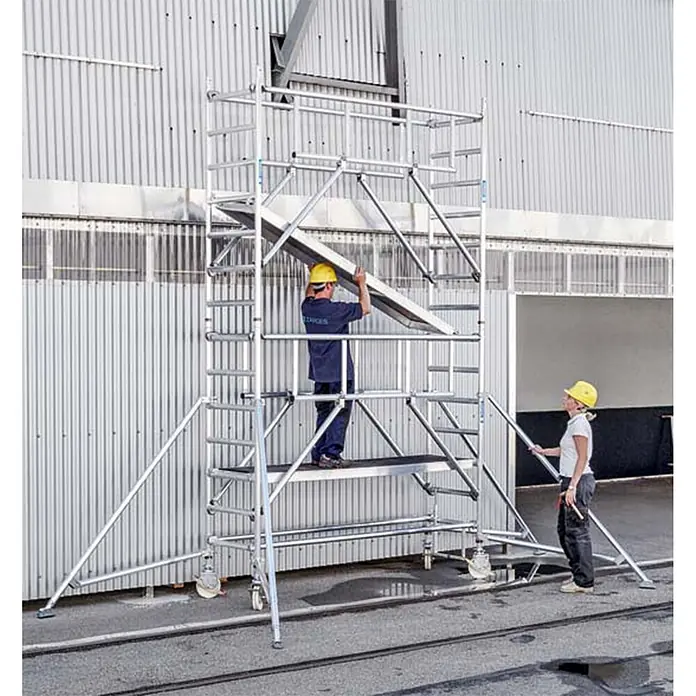 Zarges Fahrgerüst MultiTower S-PLUS 1T mit Auslegern 2,50m Plattformlänge 9,25m AH -  - Zwei Arbeiter montieren ein hohes, silbernes mobiles Aluminium-Fahrgerüst mit Rollen, mit mehreren Plattformen und Zugangsleitern.