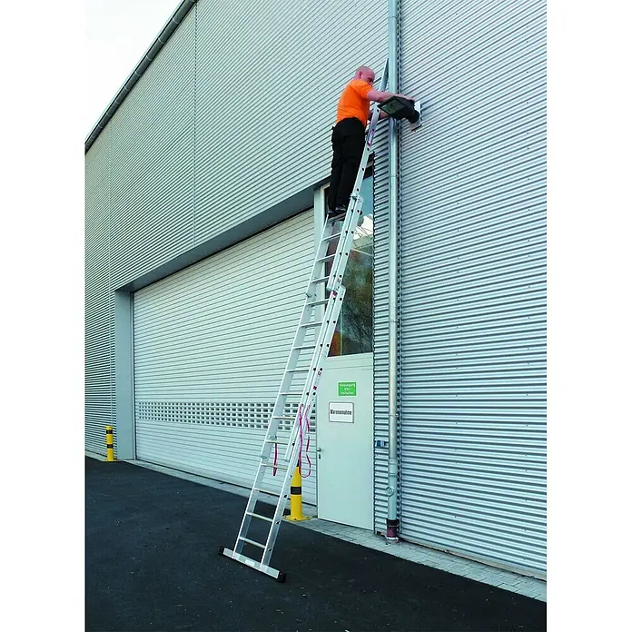 Euroline 207 Mehrzweckleiter 3x9 Sprossen -  - Ein Mann nutzt eine silberne Aluminium-Mehrzweckleiter, um an einer Leuchte an einer Gebäudewand zu arbeiten.