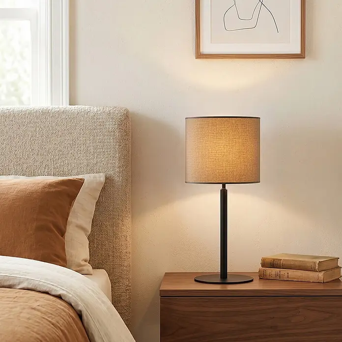Home Sweet Home Lampenschirm Bling - Ø x H: 20 x 17 cm, Castlerock, Baumwolle, Rund - Eine moderne Tischlampe mit schwarzem Fuß und hellbraunem Stoffschirm steht auf einem Nachttisch aus Holz und beleuchtet den Bereich.
