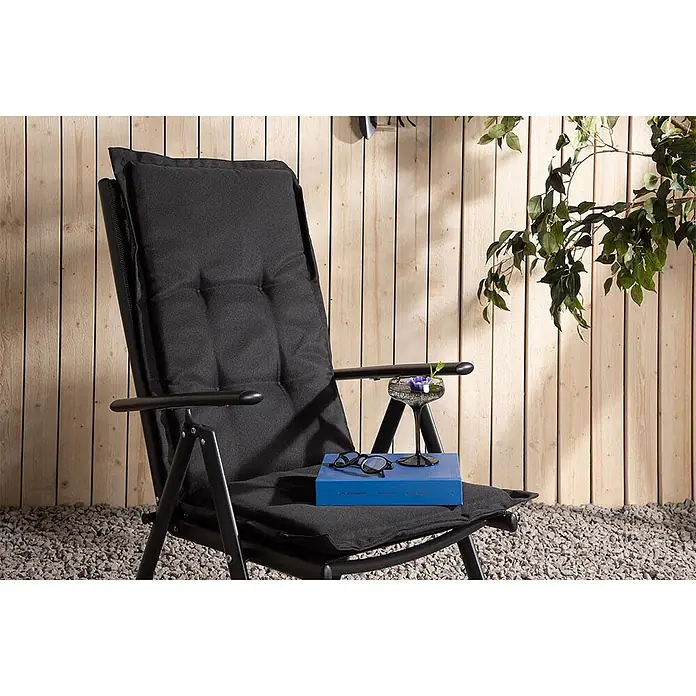 Ebuy24 Sitzauflage Cus - 1 Stk., L x B x H: 46 x 116 x 6 cm, Fasern, Schaum, Polyester., Schwarz - Schwarzer gepolsterter Klappstuhl mit Buch und Brille auf dem Sitz, in einer Außenumgebung.