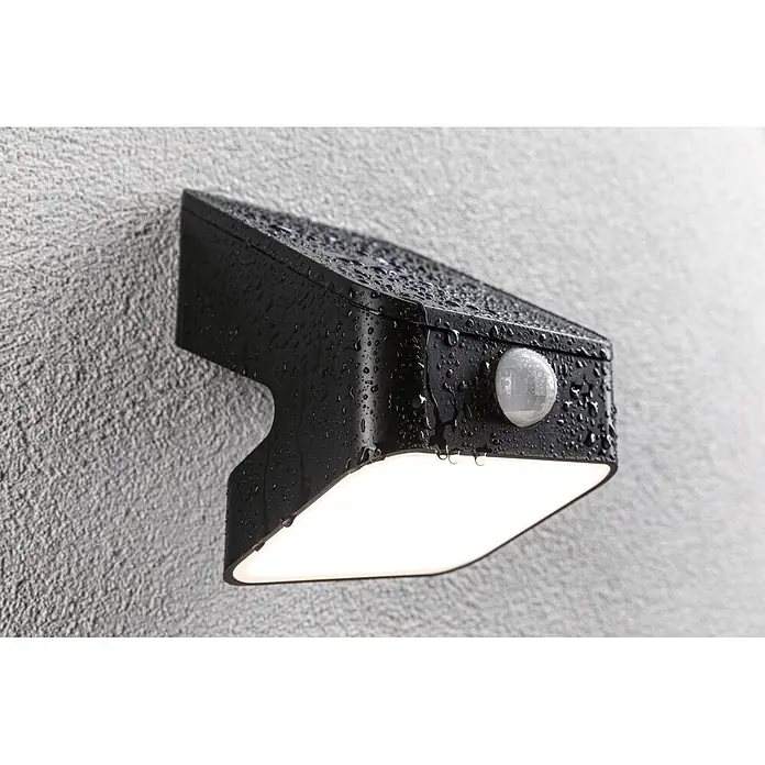 Paulmann Solarleuchte Lesly - Lichtfarbe: Warmweiß, LED, Höhe: 138 mm - Schwarze Außenwandleuchte mit integriertem Bewegungsmelder, mit Regentropfen bedeckt, leuchtend an einer strukturierten grauen Wand montiert.