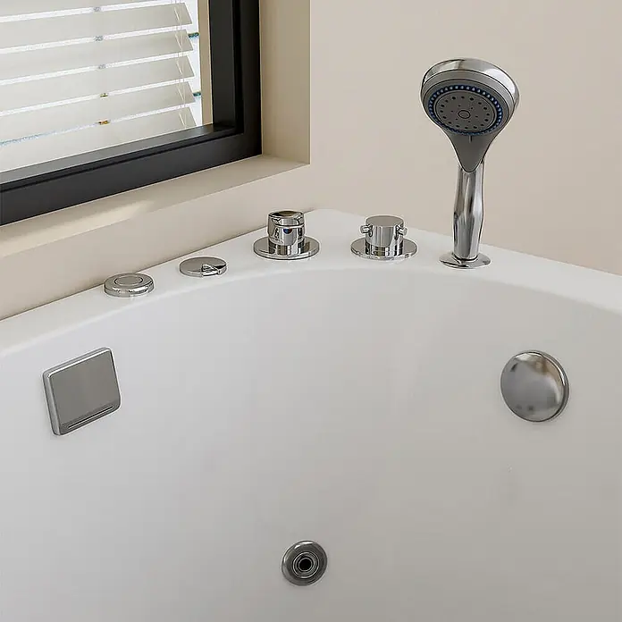 Home Deluxe Badewanne VITAL M - Weiß - Weiße Eckbadewanne mit mehreren Chromarmaturen, Handbrause, Abfluss und einer Düse, vor einer Fensterwand.