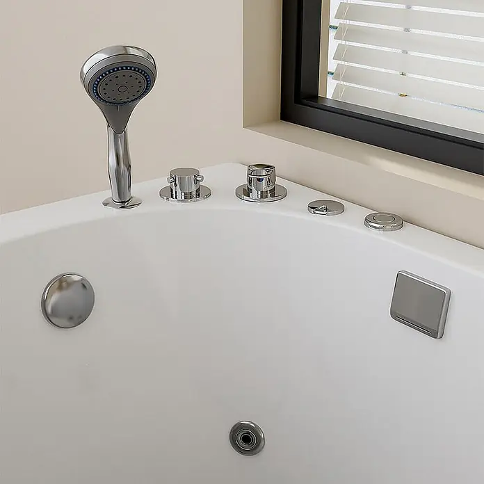Home Deluxe Badewanne VITAL M - Weiß - Weiße Eckbadewanne mit Chrom-Handbrause, Bedienknöpfen und Abfluss, in einer Badezimmerecke.