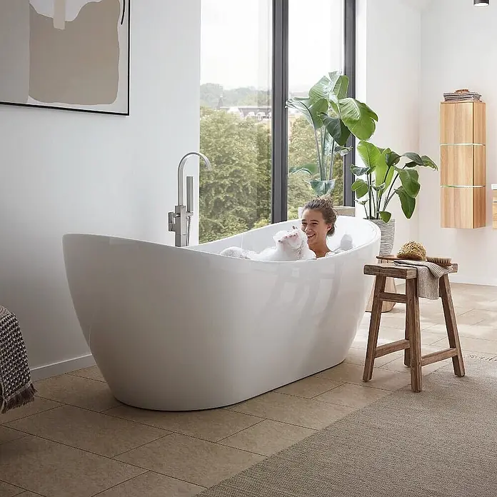 Home Deluxe Freistehende Badewanne OVALO PLUS - Weiß - Eine Frau genießt ein Schaumbad in einer eleganten weißen freistehenden Badewanne in einem hellen, modernen Bad.