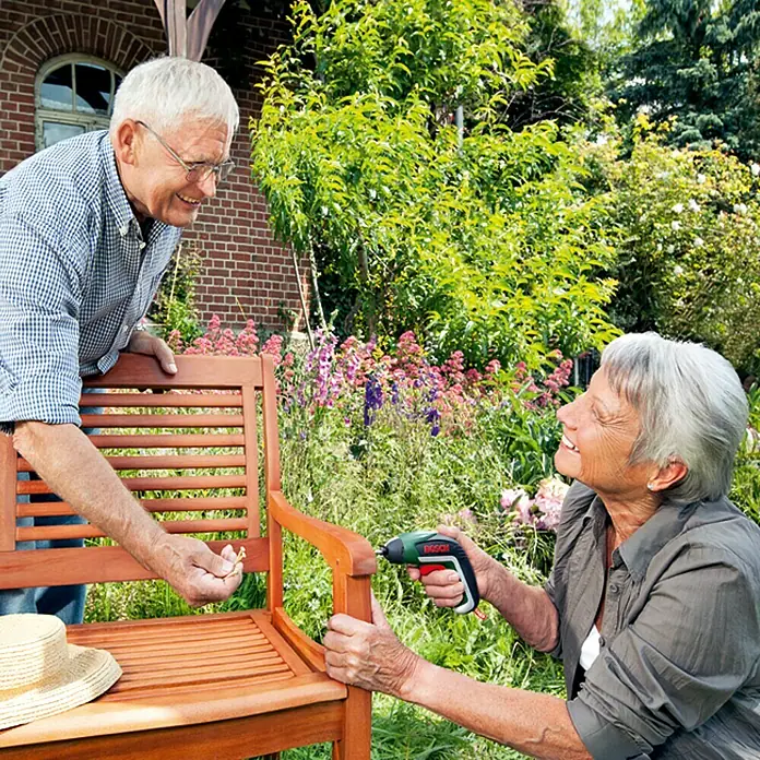 Bosch Atornillador de batería IXO Basic - 3,6 V, 1 batería, 1,5 Ah, 4,5 Nm, 10 pzs. - Una pareja de ancianos repara un banco de jardín con un destornillador inalámbrico verde de Bosch mientras trabajan en el jardín.